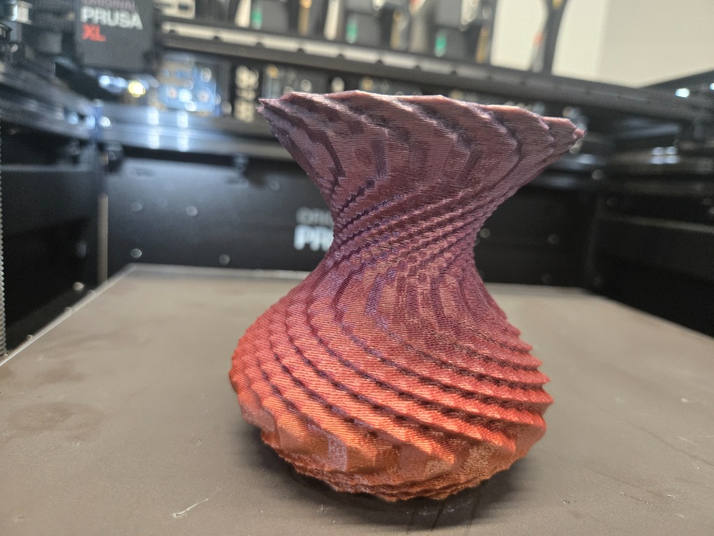 3D-printed twisted vase in copper-purple filament on a Prusa XL printer